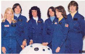 NASA’S FIRST SIX WOMEN ASTRONAUTS POSE WITH A MOCKUP OF A PERSONAL RESCUE ENCLOSURE.